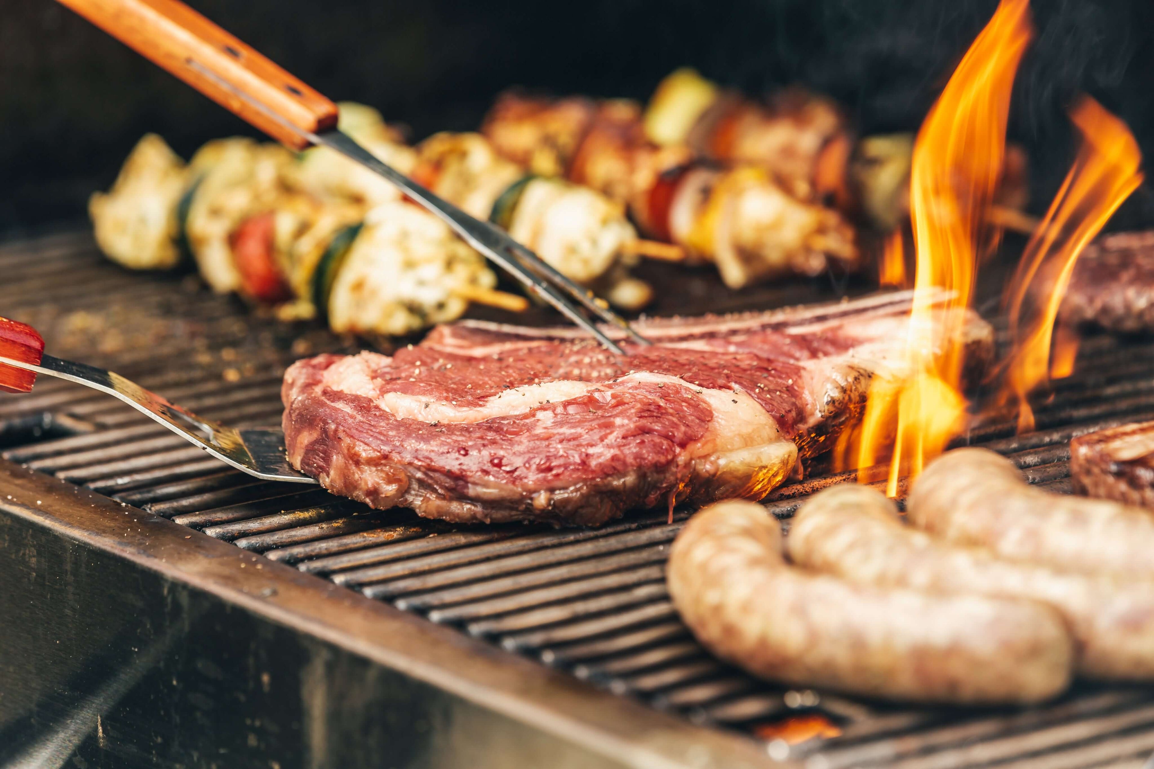 Premium firewood for braai in Cape Town: Juicy meats and steaks sizzling on a braai with flames, perfect for outdoor cooking and a smokey flavour. - Mother City has some for sale and delivery near you at the best prices. 